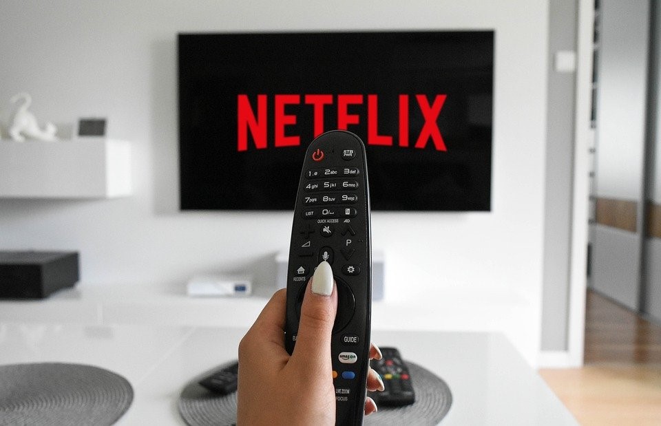 Remote control held up against a TV screen in a living room with the word 'Netflix' in red
