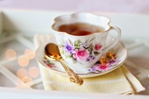 A cup of tea, with teaspoon on the plate that the cup is resting on (both have a flowery design). 